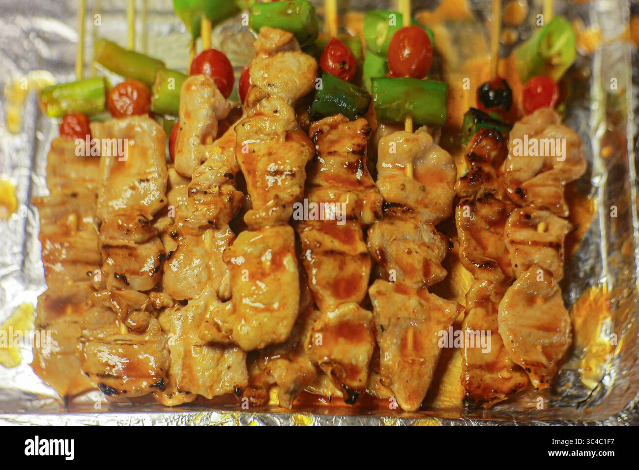 Spiedini di pollo alla griglia con salsa rossa, peperoni e pomodori. Cibo di strada tailandese esposto su un vassoio d'argento in un mercato notturno. Foto Stock