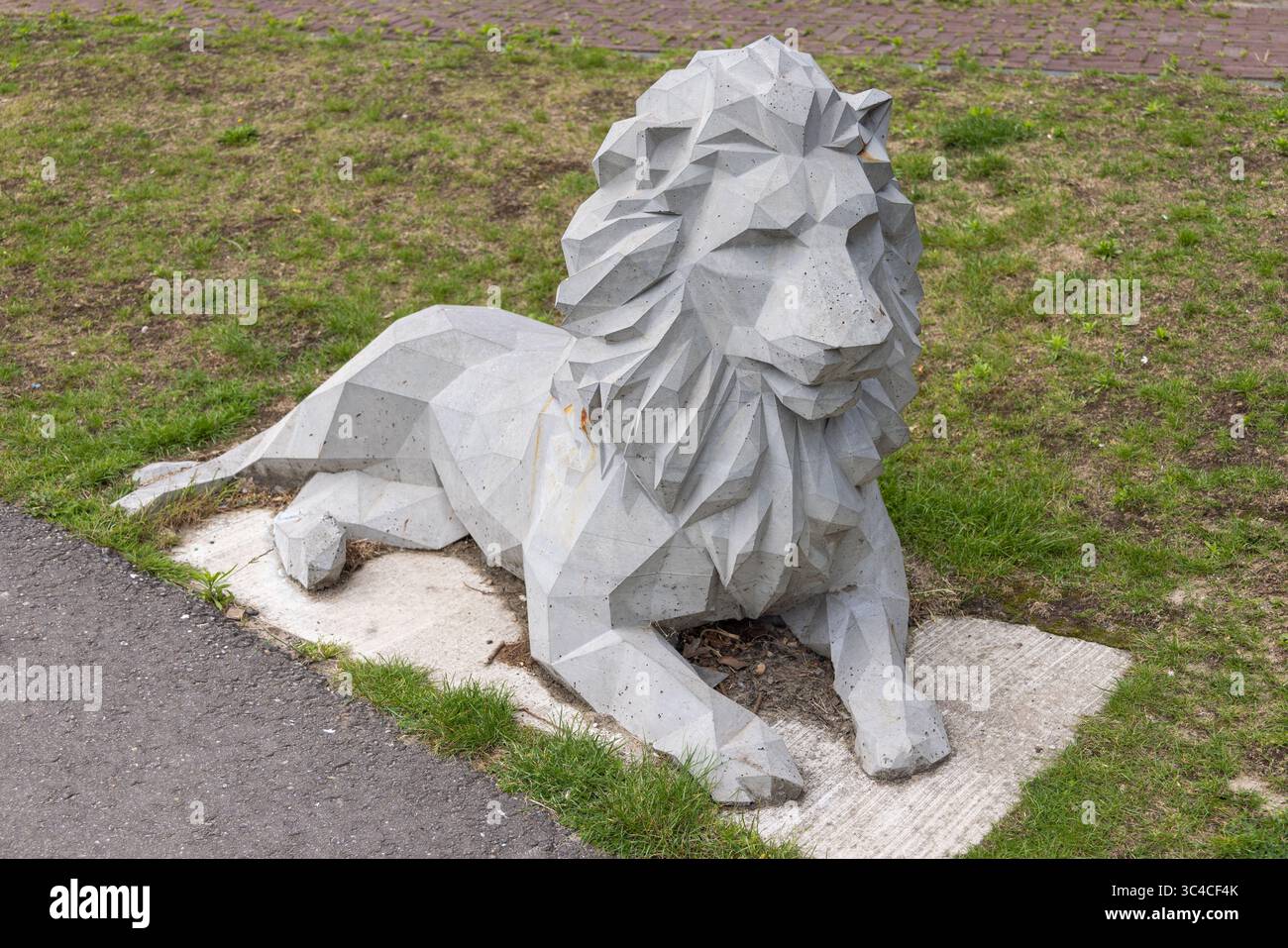 Una scultura di leone geometrica e angolare in cemento poggia su una lastra di cemento tra erba verde e un sentiero lastricato, che mostra arte pubblica moderna. Utrecht, N Foto Stock