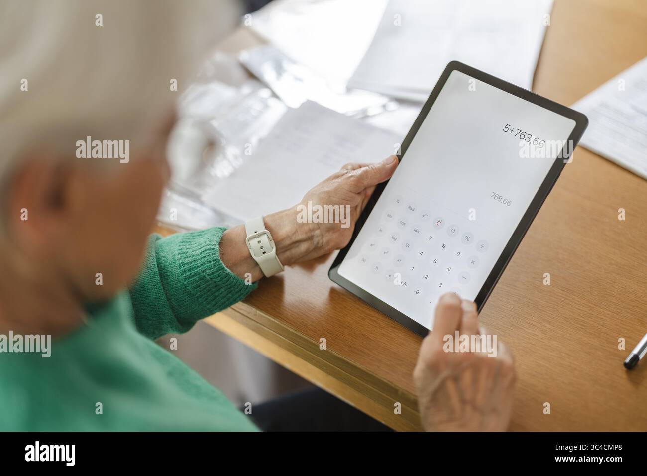 Donna anziana che usa l'app di calcolo su un tablet digitale a tavola Foto Stock