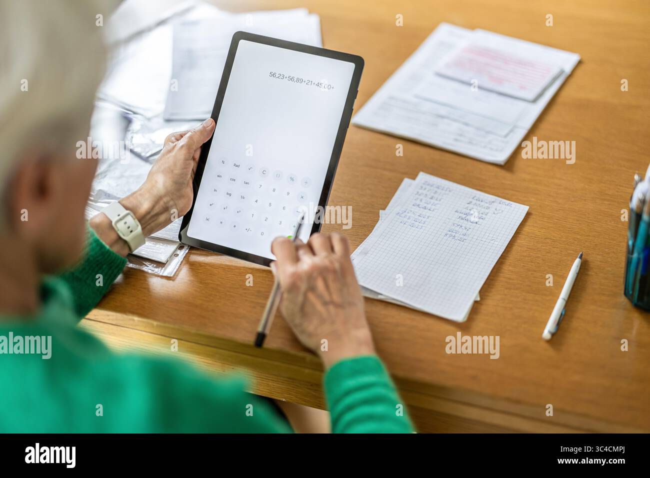 Donna anziana che usa l'app di calcolo su un tablet digitale a tavola Foto Stock