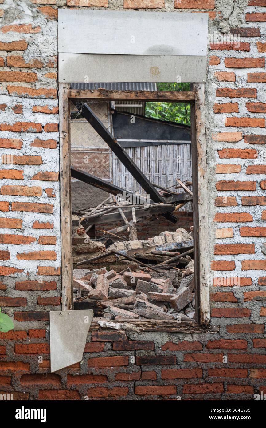 Telaio della finestra di una casa crollata senza persiane, che rivela mattoni sparsi e detriti di legno all'interno. Ideale per temi di decadimento urbano, effetti visivi catastrofici, Foto Stock