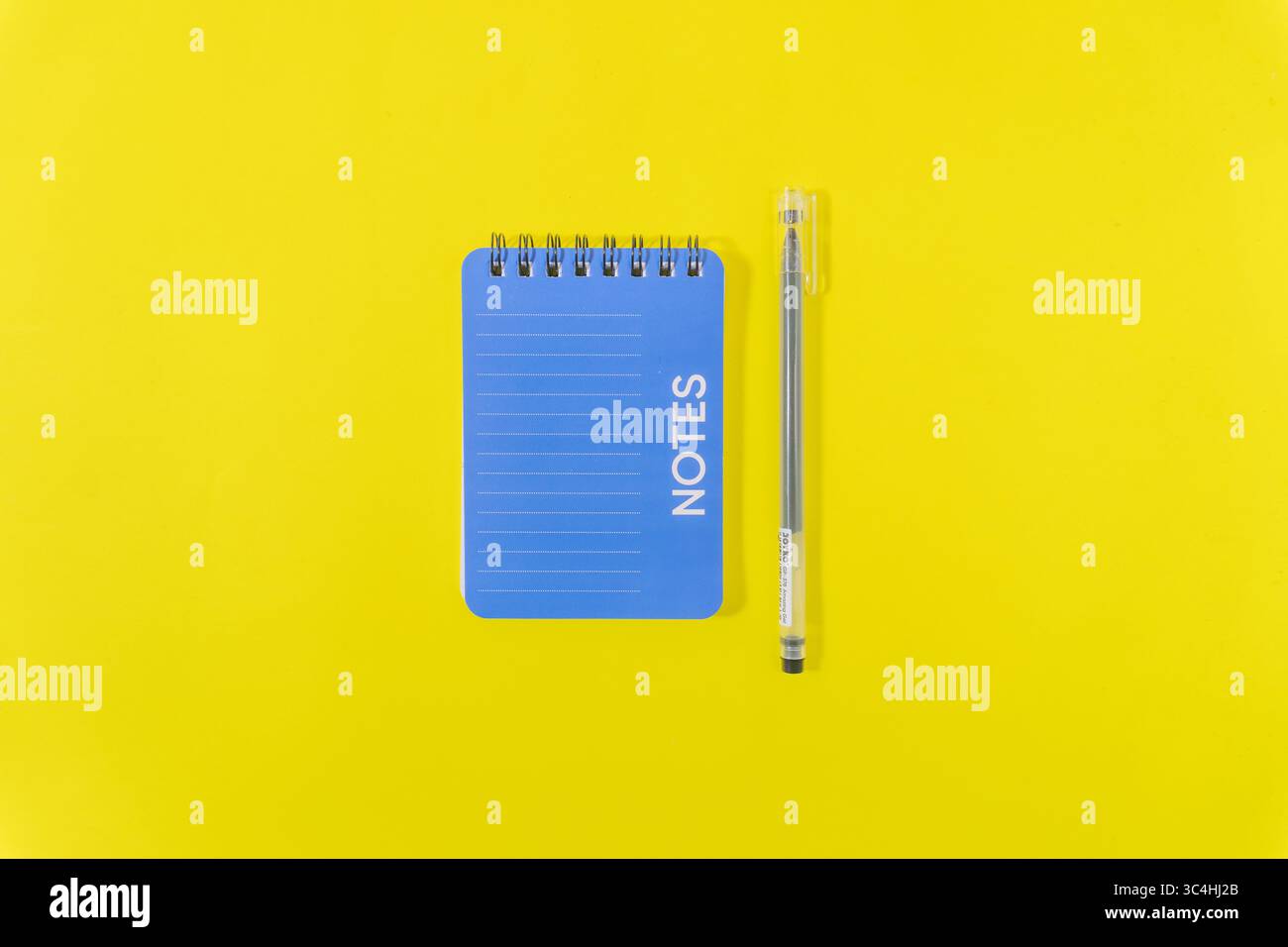 Posizione piatta di una penna e di un taccuino su uno sfondo giallo brillante. Concetto di spazio di lavoro luminoso e creativo per scrivere, scrivere e studiare Foto Stock