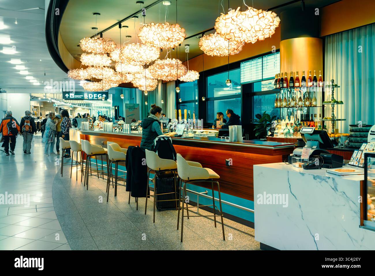 La donna siede al bancone del bar moderno con illuminazione elegante e clienti mentre passeggia all'aeroporto internazionale di Vienna. Foto Stock