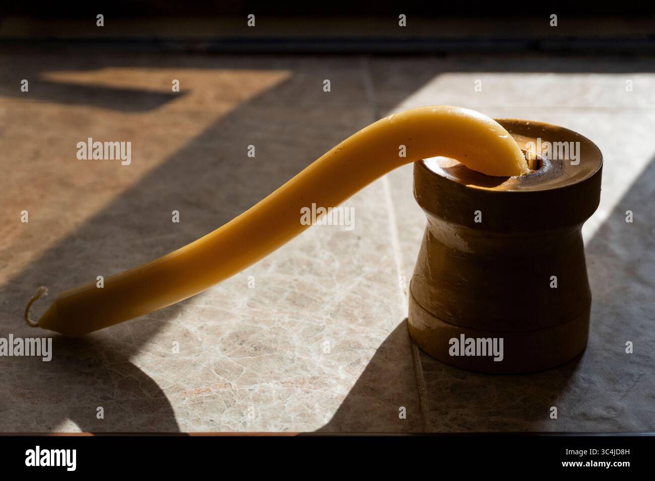 Candela gialla fusa e piegata sotto calore bruciante in un supporto di legno su una superficie piastrellata Foto Stock