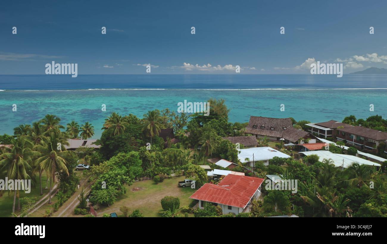 Splendida vista aerea che cattura l'idilliaco paesaggio di Tahiti con acque turchesi, vivaci barriere coralline, vegetazione lussureggiante e case tradizionali lungo la costa Foto Stock