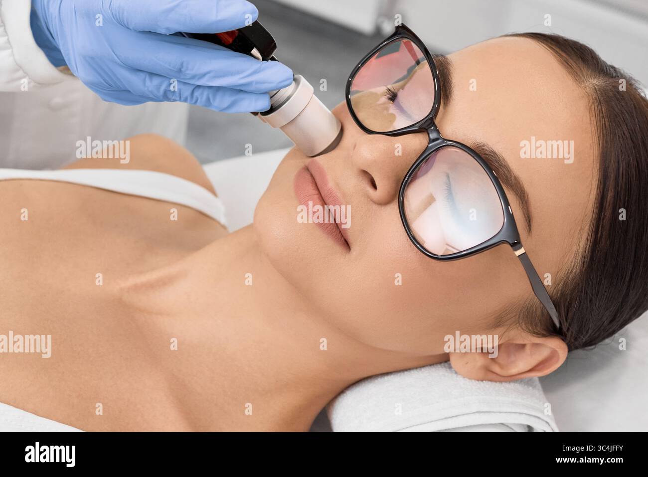 Donna attraente che indossa occhiali protettivi mentre la rimozione dei capelli laser e l'epilazione laser alla zona delle labbra sul suo viso in un salone di bellezza Foto Stock