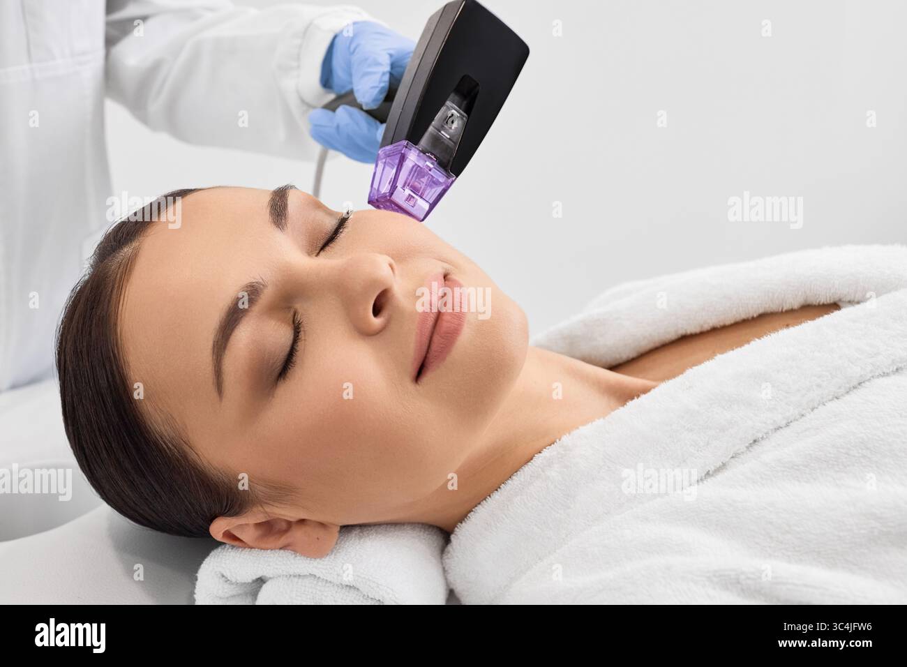 Donna mentre RF sollevamento procedura per il suo viso stringendo la pelle con cosmetologa in un salone di bellezza Foto Stock