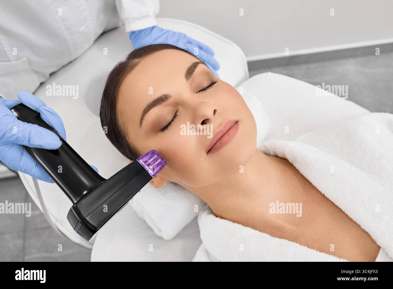 Donna brunetta che riceve la procedura di sollevamento a radiofrequenza per il suo ringiovanimento della pelle del viso presso il centro di cosmetologia Foto Stock