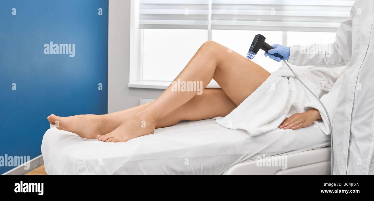 Lunghe gambe femminili durante la procedura di sollevamento della pelle a radiofrequenza con estetista in salone termale. Sollevamento RF della pelle delle gambe Foto Stock