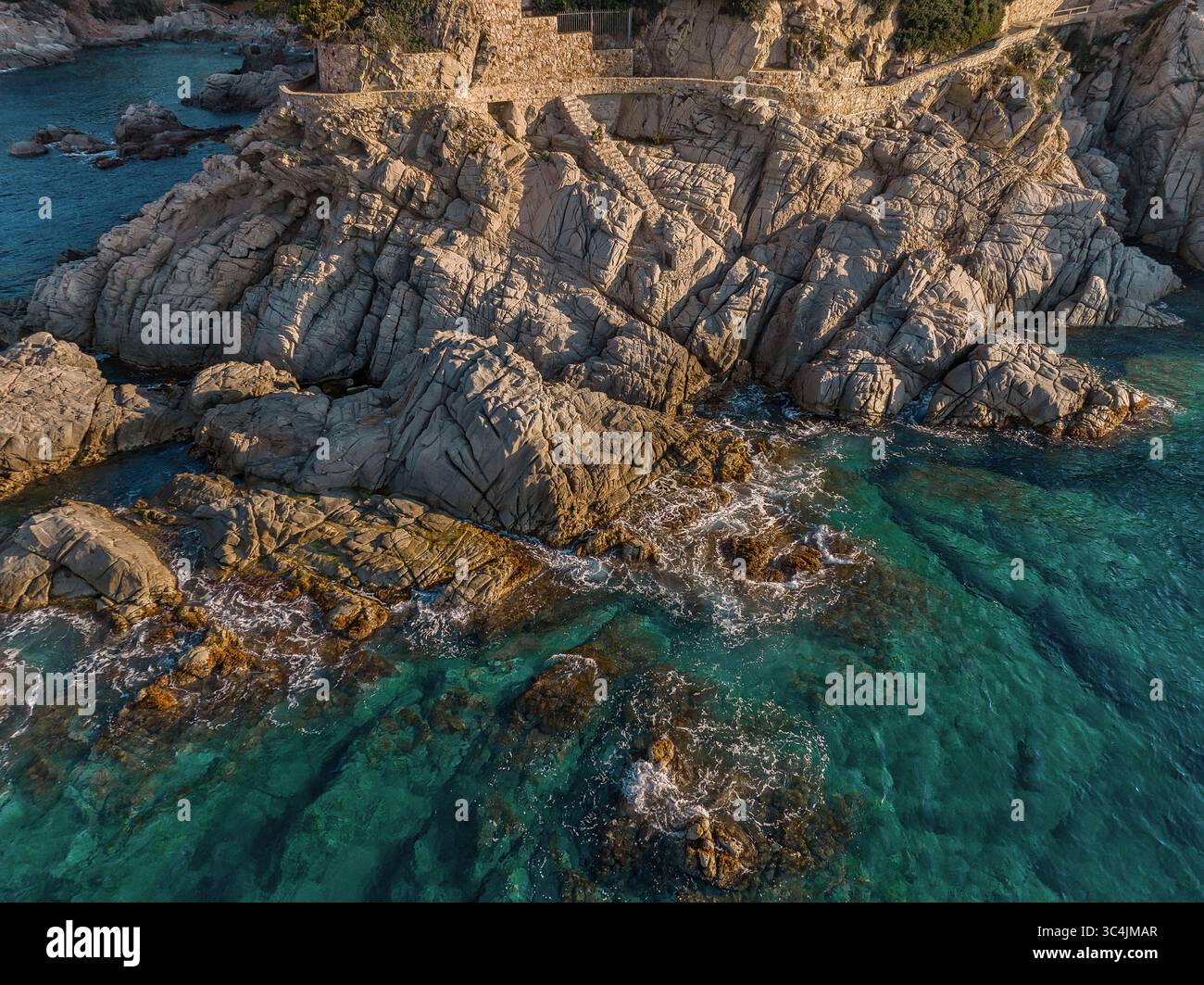 Vista aerea delle aspre scogliere che incontrano il mare turchese, le onde che si infrangono contro le rocce, creando un'affascinante scena costiera, Lloret de Mar, Catalogna, Spagna. Foto Stock