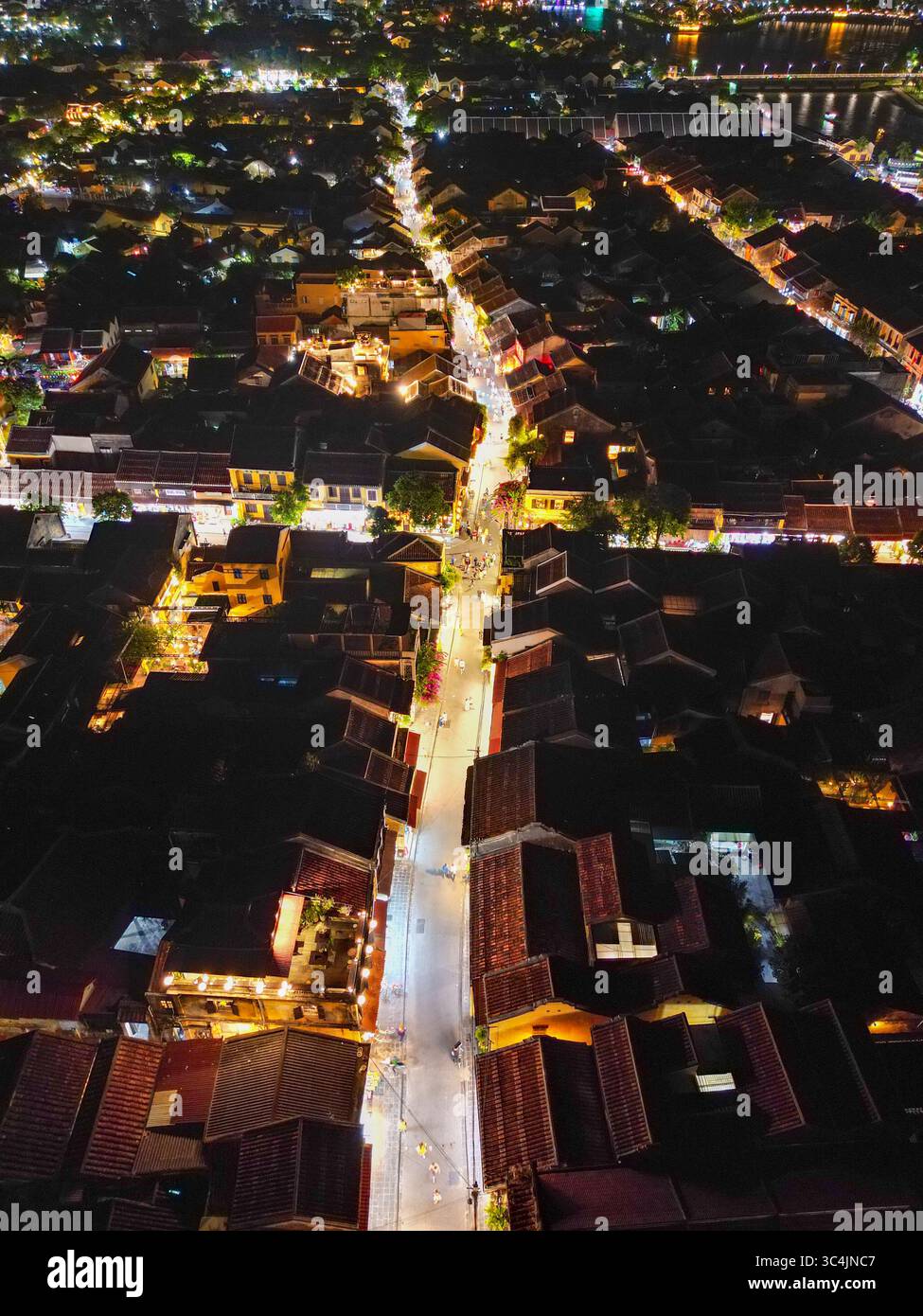 Vista aerea di una strada illuminata che attraversa la città storica, i tetti scuri contrastano con le luci vibranti, Hội An, Quảng Nam, Vietnam. Foto Stock