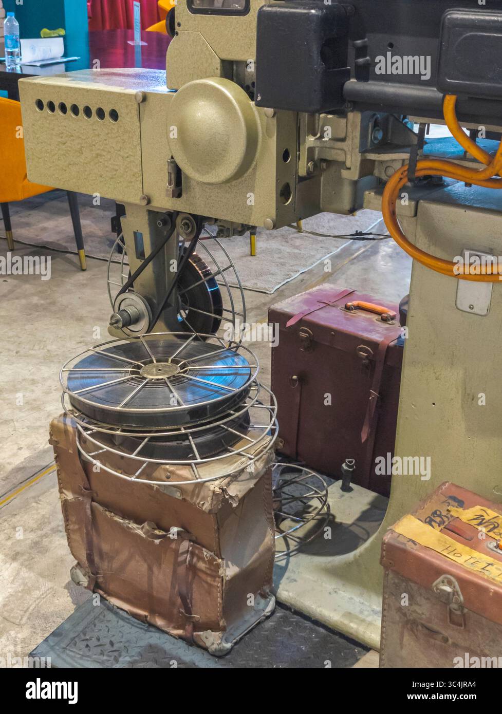 Bangkok, Thaialnd, 4 luglio 2024: Grande proiettore cinematografico professionale, circondato da vecchi rulli di pellicole e custodie in pelle vintage, in mostra nella parte principale Foto Stock