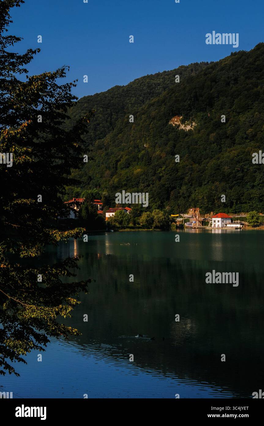 Le acque verdi di smeraldo del bacino idrico creato dall'inondazione di due bacini fluviali per lo schema idroelettrico riflettono le pendici boscose delle colline al di sotto del confine meridionale del Parco Nazionale del Triglav al massimo na Soči, regione del litorale, Slovenia. Il lago si formò alla confluenza dei fiumi Soča e Idrijca dopo la diga del Soča. Il fiume, chiamato "la bellezza di Smeraldo", sorge nelle Alpi Giulie. Foto Stock