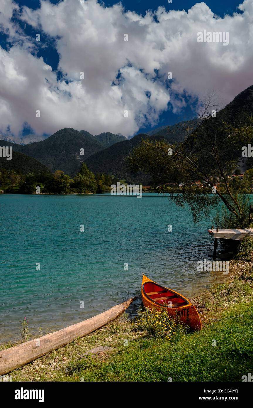 Il «Dante», una canoa arancione e giallo, contrasta con le tranquille acque verde smeraldo del bacino idrico Soci nella regione litorale della Slovenia occidentale. Vista sul lago all'inizio di settembre con nuvole che si ammassano sulle colline ricoperte di alberi sotto le vette delle Alpi Giulie nel Triglav o nel Parco Nazionale di Triglavski. Foto Stock