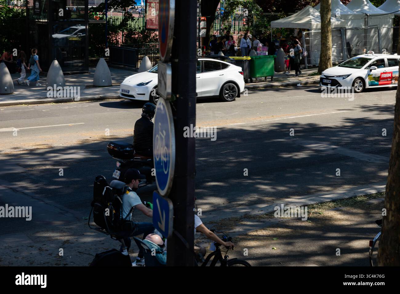 Ripresa ad angolo alto di una scena stradale della città, con una Tesla bianca e un taxi, uno scooter con portabicchieri e ciclisti. La luce del sole proietta ombre attenuate. Foto Stock