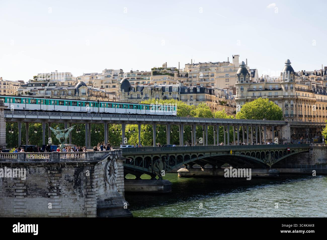 Una scena di ponti parigini: Un treno della metropolitana color tè attraversa una struttura storica, pedoni passeggiano lungo il suo passaggio pedonale e formano eleganti edifici parigini Foto Stock
