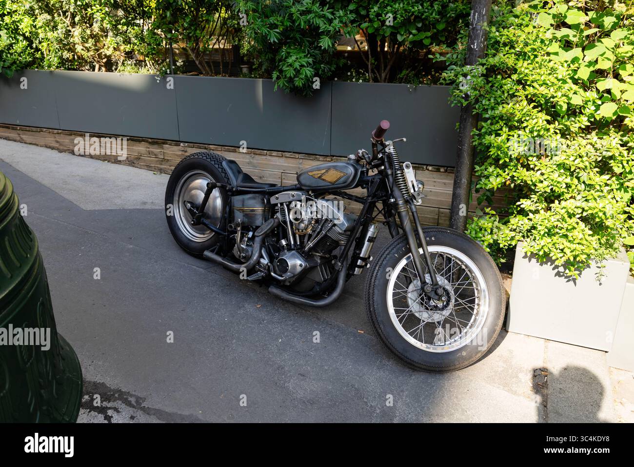Una moto d'epoca personalizzata, parcheggiata su una strada cittadina, crogiola alla luce del sole. La finitura grigio metallizzato e i grandi pneumatici creano un'estetica urbana di tendenza. IDE Foto Stock