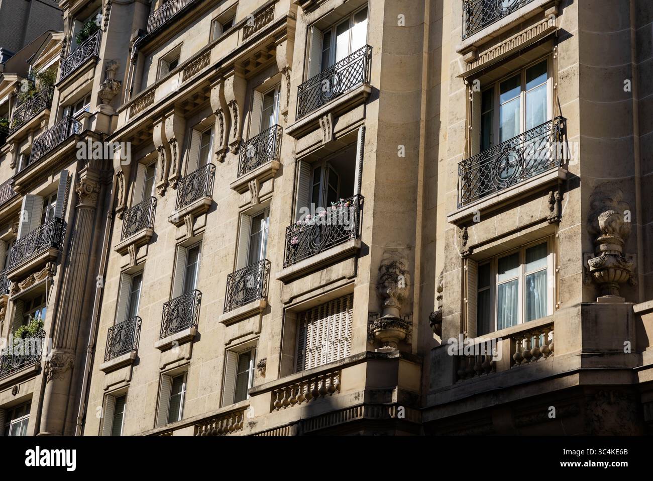 Una facciata di un edificio di appartamenti parigino soleggiato che presenta balconi ornati con intricate ringhiere in ferro battuto. Eleganti lavori in pietra e architetture Foto Stock