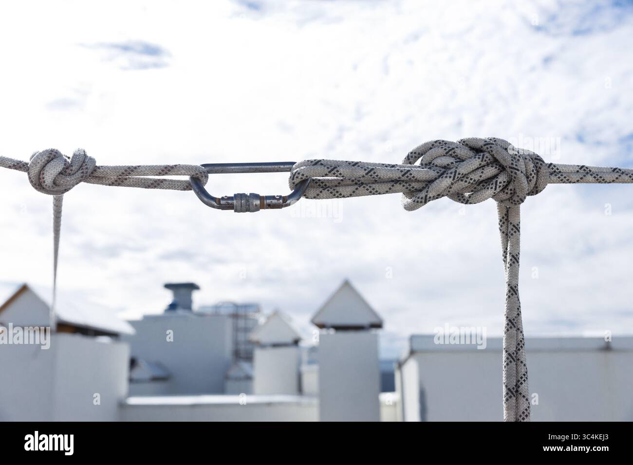 Primo piano di un nodo legato in una corda resistente collegata in modo sicuro a un moschettone sul tetto contro un cielo nuvoloso in una luce naturale brillante Foto Stock