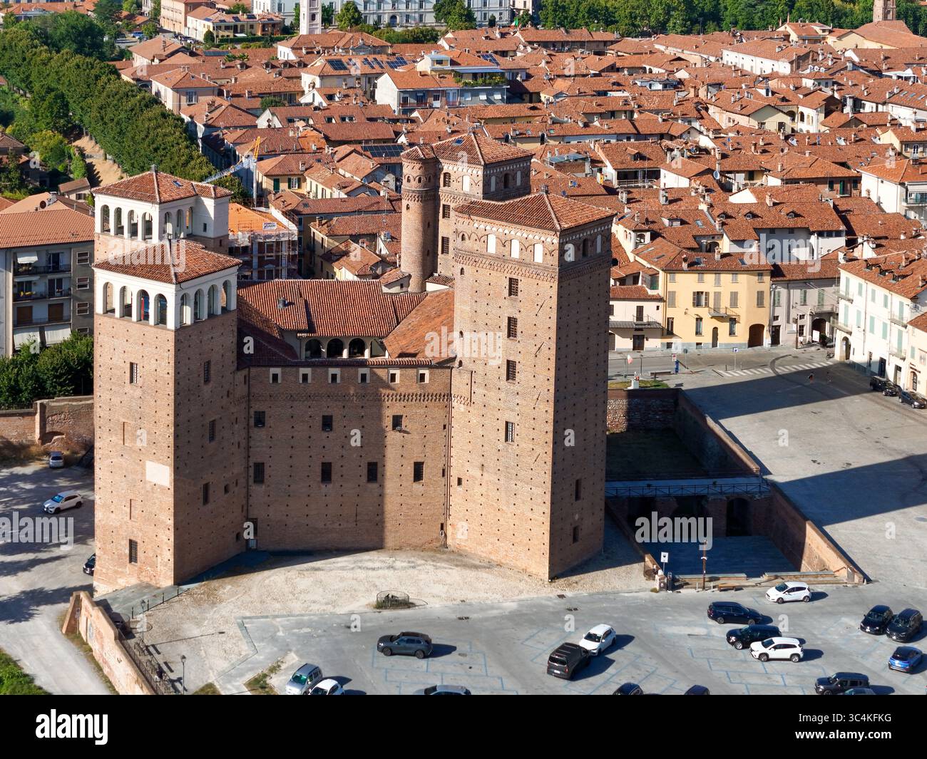 Veduta aerea dell'imponente Castello degli Acaja, una fortezza medievale con le sue robuste torri in mattoni, si erge orgogliosamente sullo sfondo dei tetti in terracotta di Fossano, Fossano, Piemonte, Italia. Foto Stock