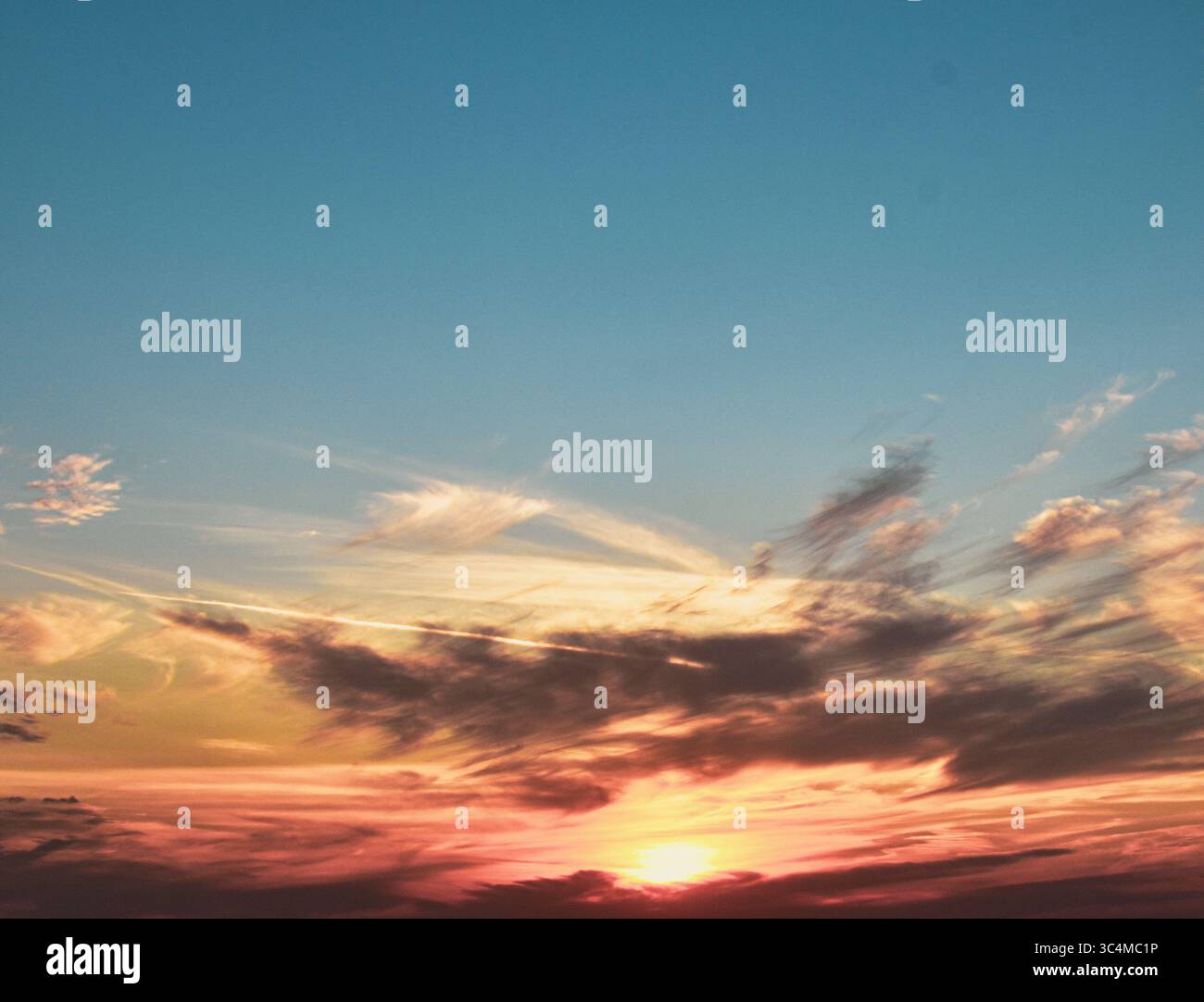 Il sole della sera si tuffa dietro le nuvole, illuminando il cielo con tonalità di arancione, giallo e grigio vivaci. Foto Stock