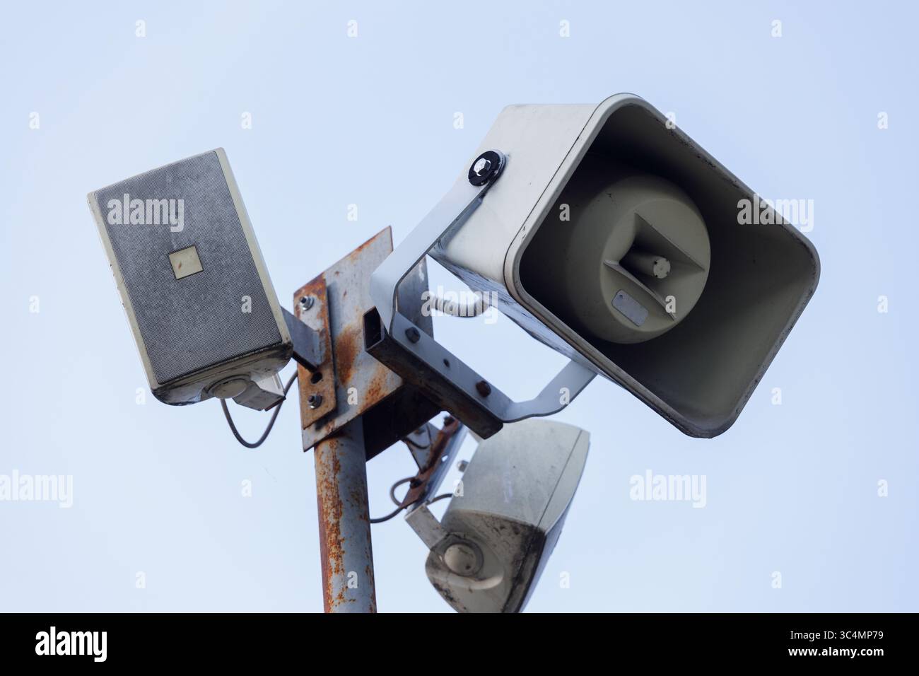 Un array multiforme di altoparlanti per esterni montati su un palo metallico contro un cielo blu chiaro, che mostra il design e la funzionalità di Public Address Foto Stock