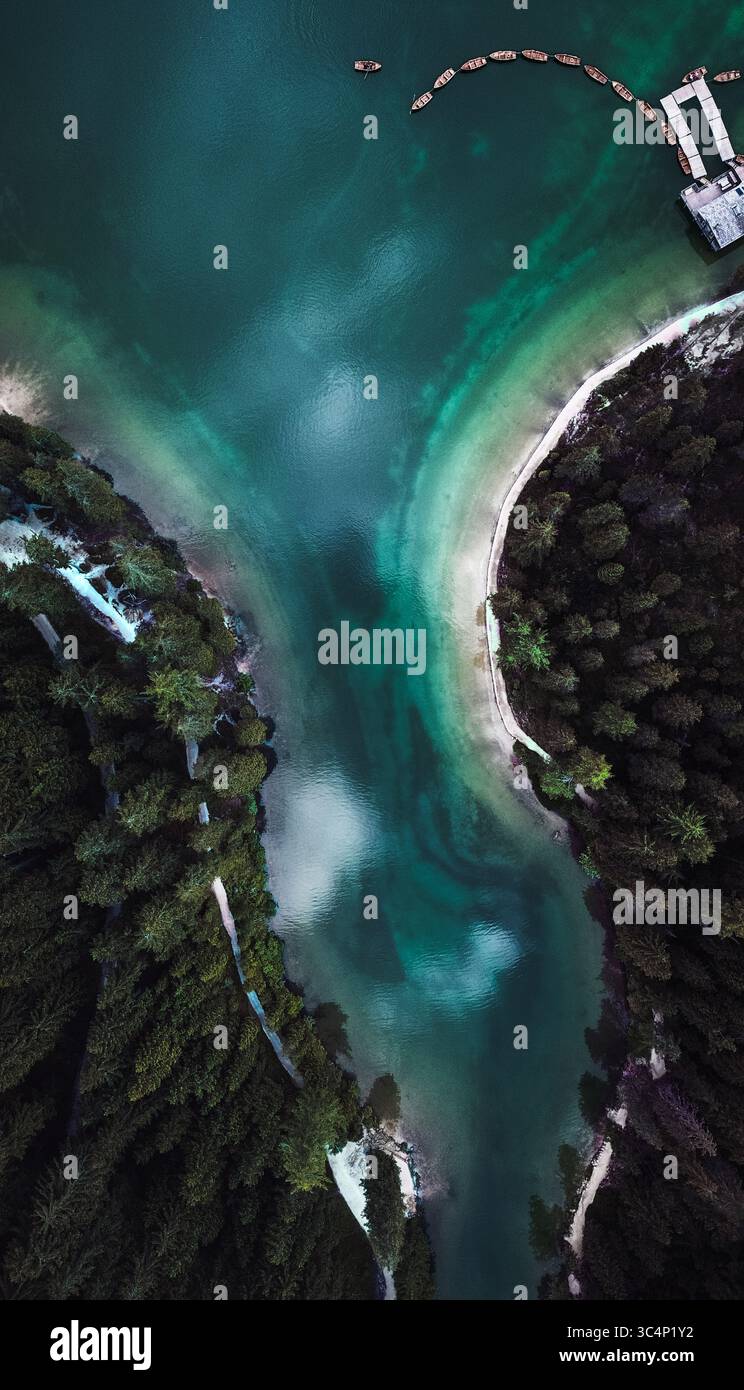 Vista aerea delle profonde acque turchesi che si snodano contro le rive sabbiose del Lago di Braies, abbracciate da fitte foreste sempreverdi, Braies, Trentino-alto Adige, Italia. Foto Stock