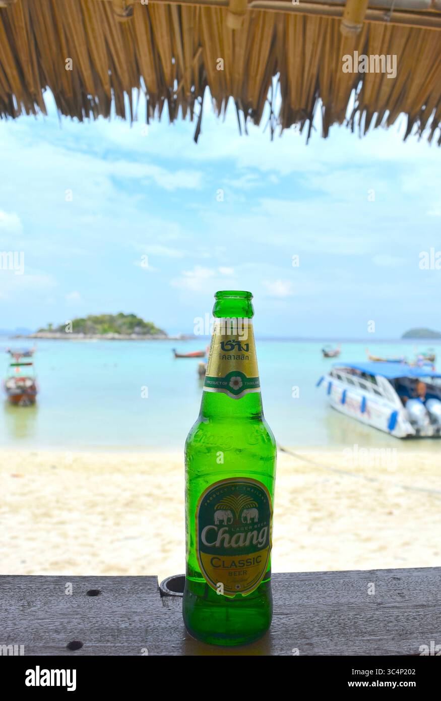 Bottiglia di birra tailandese Chang su un tavolo di legno che si affaccia sulla splendida spiaggia di sabbia di Koh Lipe in Thailandia. Foto Stock
