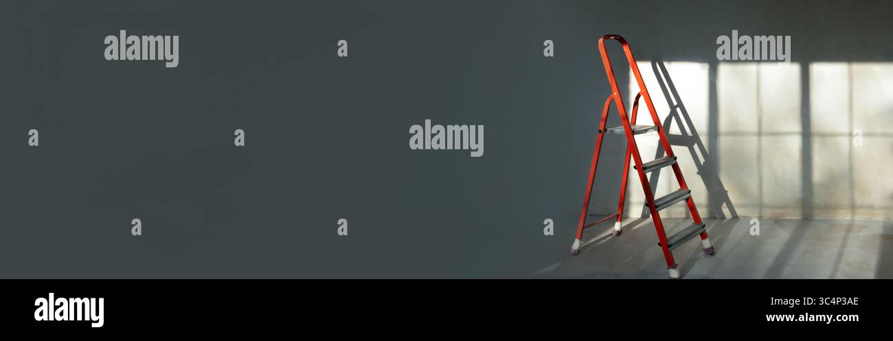 Scala a cavalletto rossa in camera vuota, senza lavori di ristrutturazione. sfondo grigio. Concetto di riparazione Foto Stock