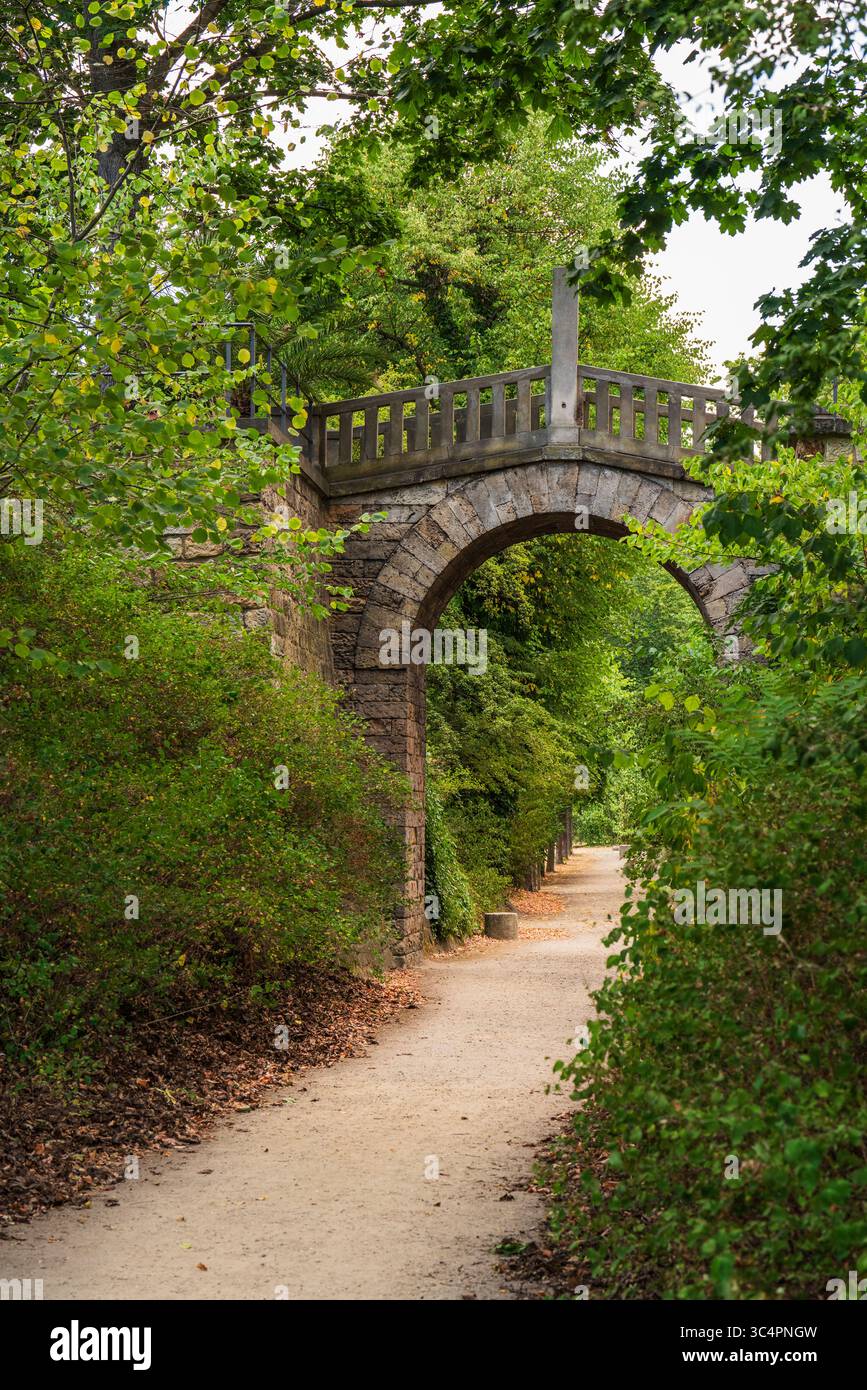 L'arco in pietra con ponte in legno attraversa il sentiero pedonale in un tranquillo parco. Ambiente naturale sereno, ideale per viaggi, architettura, paesaggio, esterni Foto Stock