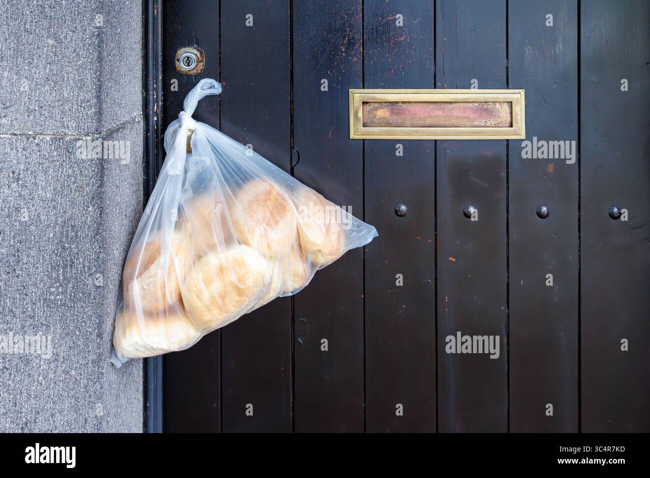 Un sacchetto di plastica con cuccioli rotondi appesi alla maniglia di una porta anteriore in legno. Porta d'ingresso alla casa. Foto di alta qualità Foto Stock