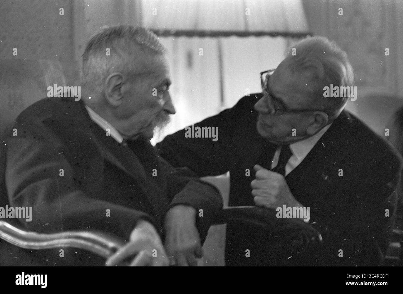 Incontro di figure di alto livello tra cui (ministro) Jelle Zijlstra Whizgle News, Dutch Desk, Paesi Bassi, 1950-2000 due anziani si impegnano in una conversazione profonda, uno ascoltando intensamente mentre l'altro parla con un'espressione premurosa. L'ambiente suggerisce un'atmosfera calda e intima, impreziosita da luci soffuse e arredi confortevoli. Foto Stock