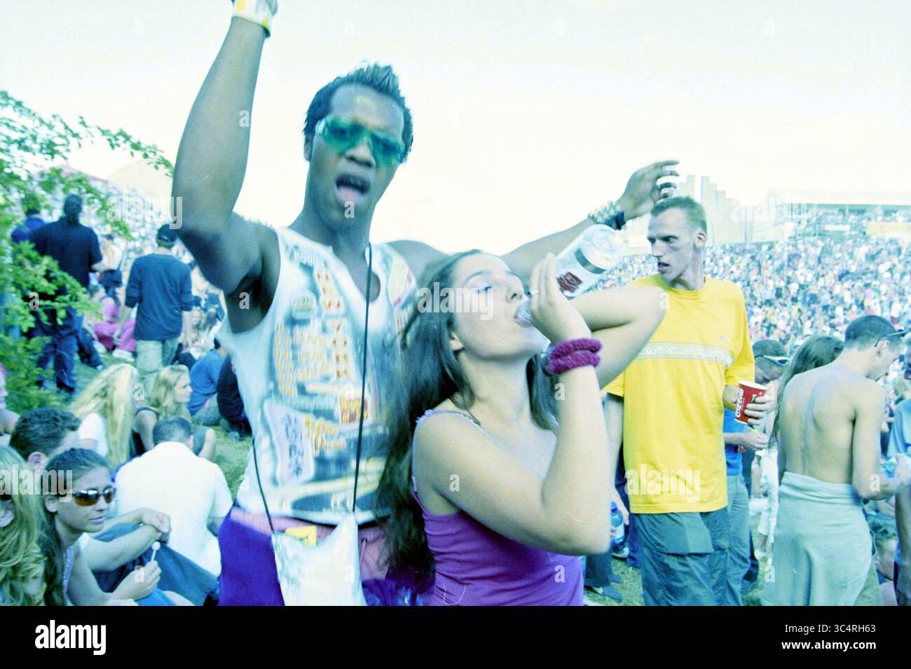 Dance Valley Goers, 03-08-2001 Whizgle News, Dutch Desk, The Netherlands, 1950-2000 Un vivace raduno in un ambiente di festival, dove un giovane balla energicamente con le braccia alzate mentre una giovane donna nelle vicinanze sorseggia da una bottiglia d'acqua. La folla intorno a loro è vibrante e impegnata, godendosi l'atmosfera festosa. Foto Stock