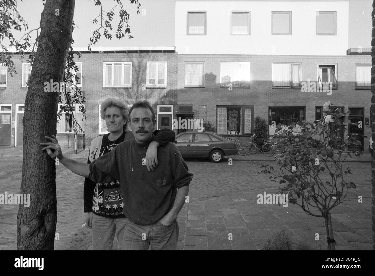 Piano della casa della famiglia Deventer, 05-12-1991 Whizgle News, Dutch Desk, Paesi Bassi, 1950-2000 due persone si trovano di fronte a un edificio, in posa casuale con uno che poggia un braccio sulla spalla dell'altro. Lo sfondo presenta un mix di finestre e verde, creando una rilassata scena urbana. Foto Stock
