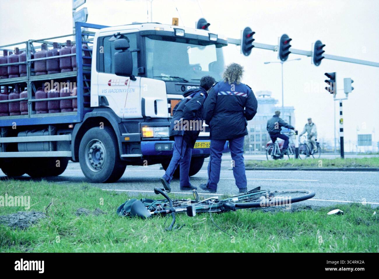 Accident, Kruisweg, Hoofddorp, Kruisweg, Paesi Bassi, 14-01-1999 Whizgle News, Dutch Desk, Paesi Bassi, 1950-2000 due persone in giacche esaminano una bicicletta stesa a terra vicino a un camion fermo che trasporta bombole di gas. Sono visibili più semafori e i ciclisti possono essere visti sullo sfondo. Foto Stock