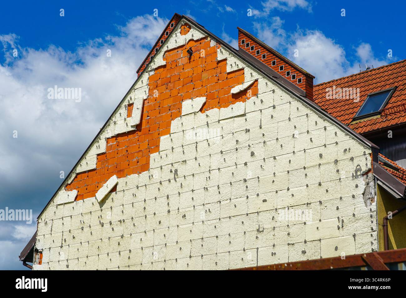 Facciata di una casa con isolamento danneggiato dal vento che espone mattoni rossi sotto, mostrando vulnerabilità strutturale Foto Stock