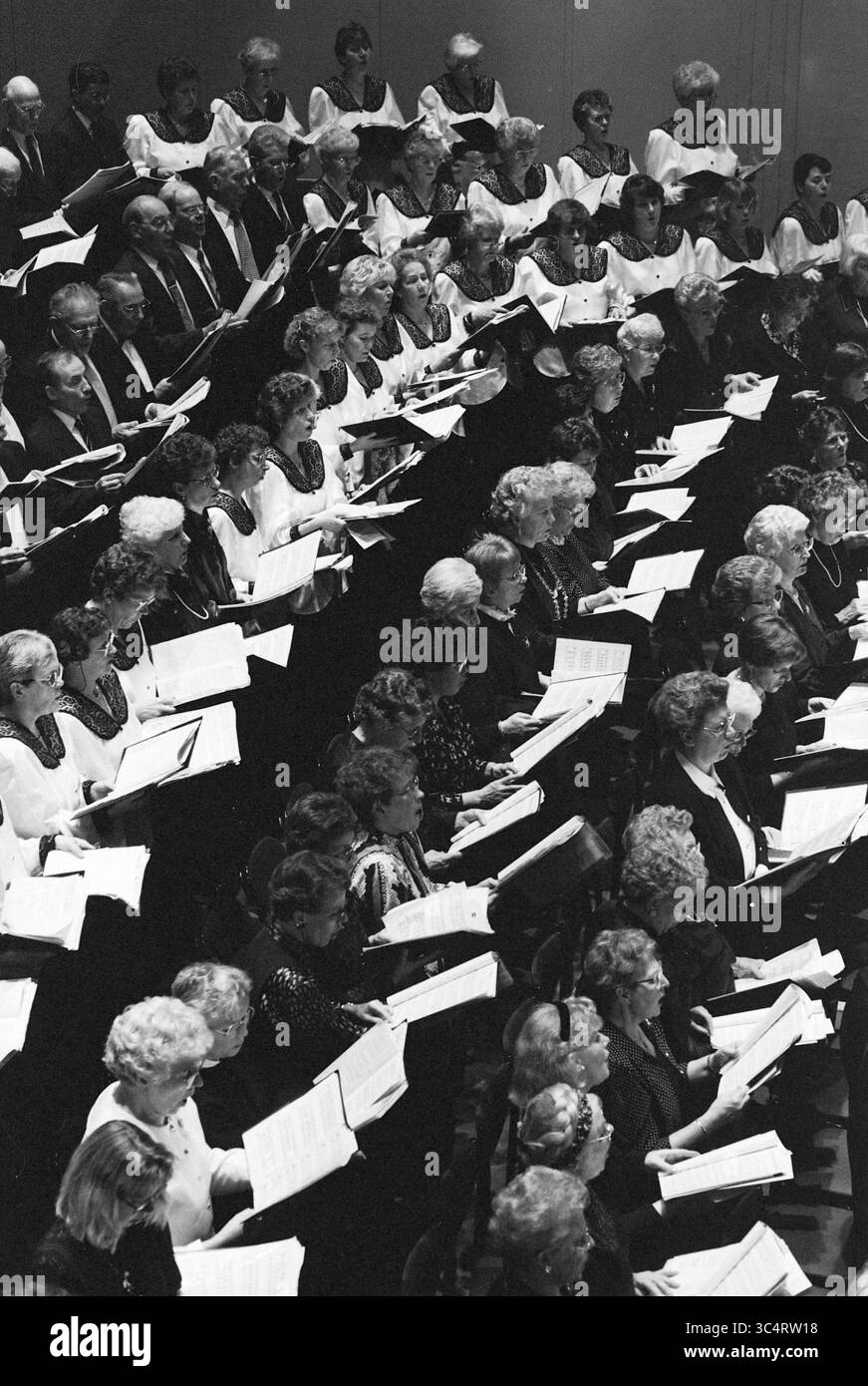 Canto natalizio, Concertgebouw, 21-12-1993 Whizgle News, Dutch Desk, Paesi Bassi, 1950-2000 Un grande gruppo di cantanti, vestiti in abbigliamento formale, è impegnato in una performance corale. Sono concentrati sui loro spartiti musicali, creando un senso di armonia e dedizione. La disposizione include uomini e donne con diverse acconciature, ognuna delle quali contribuisce all'arte collettiva dello spettacolo. Foto Stock
