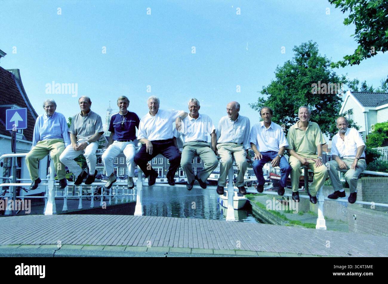 Gruppo di relatori Haarlems Dagblad Football, 28-08-2002 Whizgle News, Dutch Desk, Paesi Bassi, 1950-2000 Un gruppo di dieci uomini più anziani si mette in posa, apparentemente galleggiando a mezz'aria mentre si siede sul bordo di un ponte. Sullo sfondo, un pittoresco canale e pittoreschi edifici si aggiungono alla suggestiva scena. Gli uomini mostrano un mix di espressioni, dai sorrisi alle risate, mostrando insieme un momento divertente e spensierato. Foto Stock