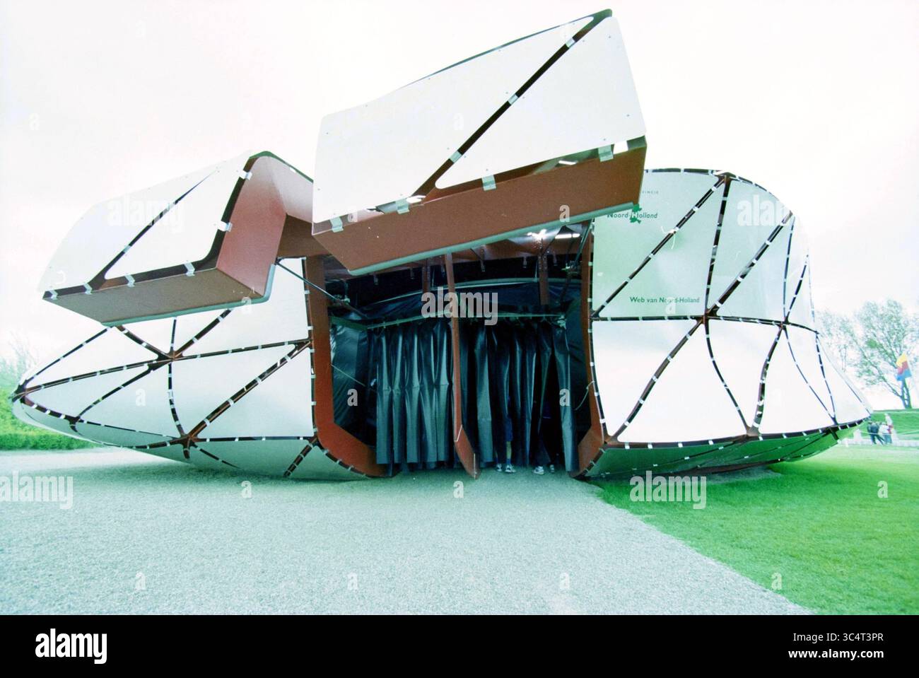 Padiglioni esterni Haarlemmermeer, 24-04-2002 Whizgle News, Dutch Desk, Paesi Bassi, 1950-2000 Una suggestiva struttura architettonica caratterizzata da un distintivo design angolare con superfici riflettenti e un'invitante entrata, circondata da lussureggiante vegetazione. La forma innovativa è caratterizzata dalla sua apertura e dalla geometria dinamica, creando un forte impatto visivo. Foto Stock