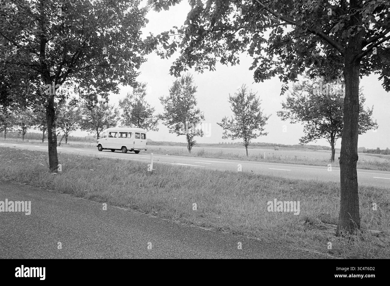 Panoramica della posizione del tunnel Wijkermeer, Overviews, 28-07-1983 Whizgle News, Dutch Desk, Paesi Bassi, 1950-2000 Un pulmino d'epoca percorre una strada tortuosa, fiancheggiata da una fila di alberi da un lato e da campi aperti dall'altro, creando un'atmosfera di campagna serena. Foto Stock