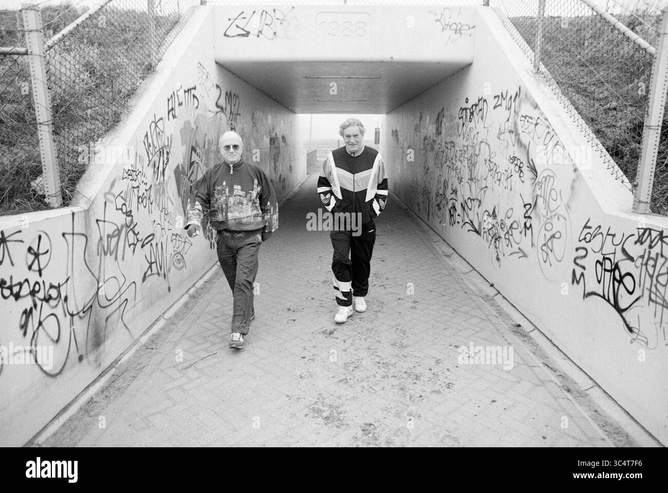 Winter Walk, 13-02-1993 Whizgle News, Dutch Desk, The Netherlands, 1950-2000 due persone camminano fianco a fianco attraverso un sottopassaggio coperto di graffiti, che mette in mostra un mix di stile informale e ambiente urbano. I vivaci disegni sulle pareti contrastano con il loro comportamento rilassato mentre condividono un momento insieme. Foto Stock