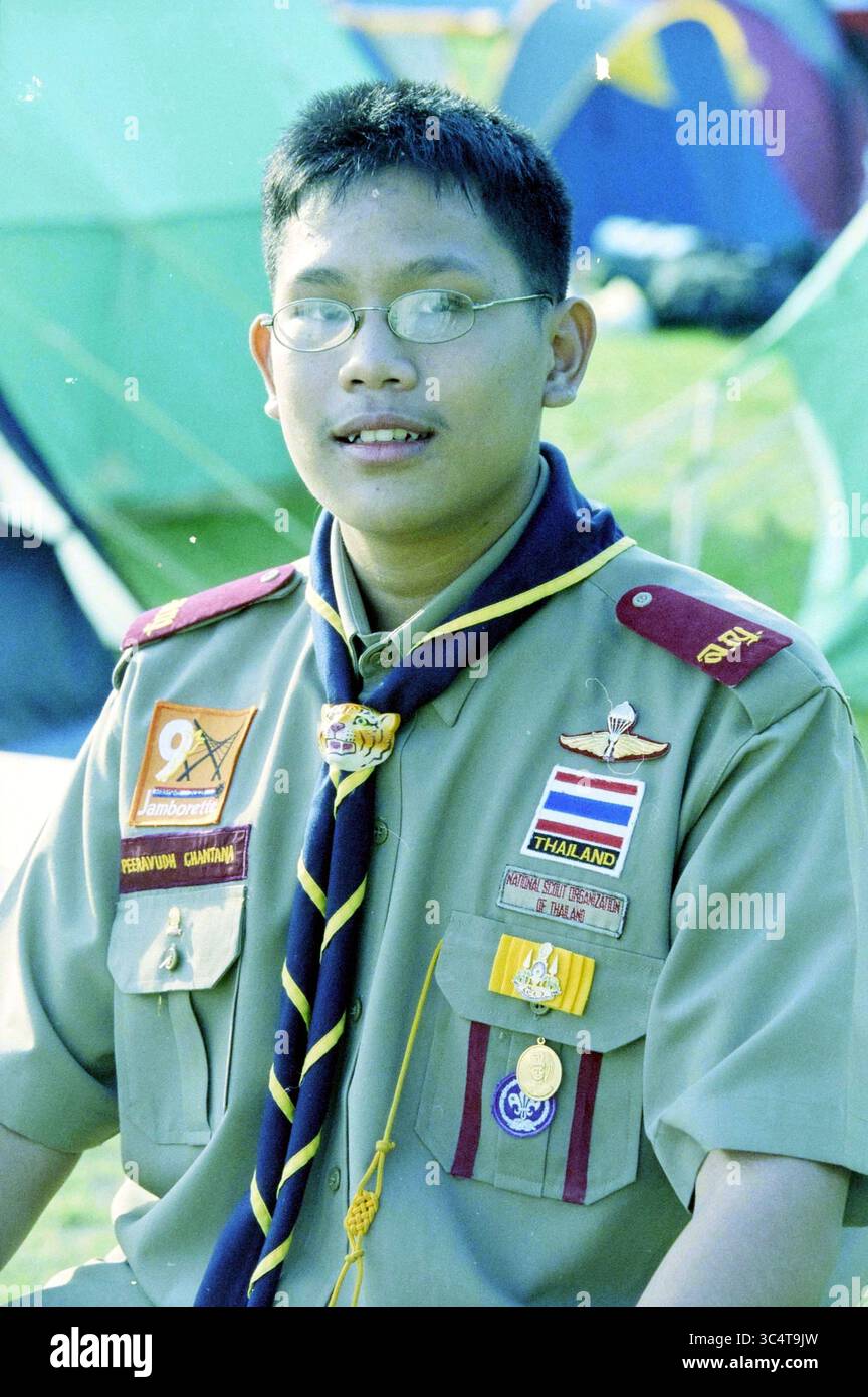 Jamborette, Spaarnwoude, Spaarnwoude, 26-07-2003 Whizgle News, Dutch Desk, i Paesi Bassi, 1950-2000 Un giovane scout siede con un sorriso amichevole, indossando un'uniforme ben pressata ornata da vari stemmi e un colorato capo collo. Dietro di lui, le tende sono collocate in un ambiente ricreativo all'aperto, suggerendo un campeggio o un evento scout. Foto Stock