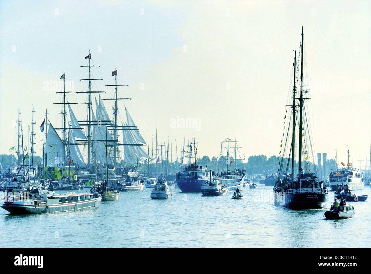 Sail Parade 200 IJmuiden [2000], IJmuiden, Paesi Bassi, 23-08-2000 Whizgle News, Dutch Desk, i Paesi Bassi, 1950-2000 Una vivace scena caratterizzata da una serie di maestose navi a vela e piccole imbarcazioni che navigano in un vivace porto, con bandiere che sventolano nella brezza e alberi che fiancheggiano la costa lontana. Foto Stock