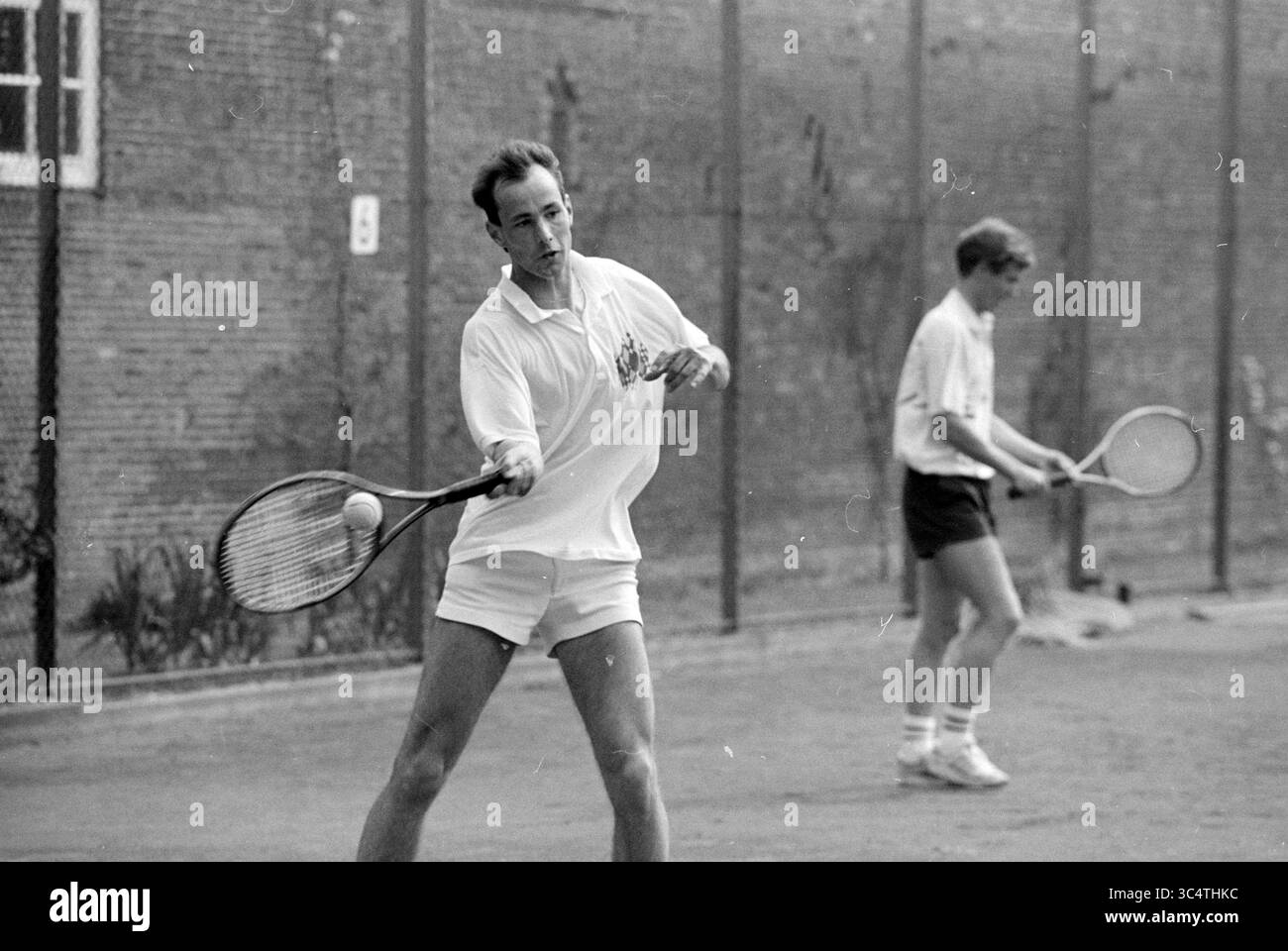 Inizio della stagione del tennis, H'stede, Heemstede, Paesi Bassi, 11-04-1992 Whizgle News, Dutch Desk, Paesi Bassi, 1950-2000 due uomini si impegnano in una partita di tennis su un campo. Un giocatore è a metà corsa, pronto a colpire la palla, mentre l'altro è pronto sullo sfondo, entrambi vestiti con abbigliamento casual da tennis. L'ambientazione è caratterizzata da una recinzione e linee di campo visibili, che sottolineano la natura dinamica dello sport. Foto Stock