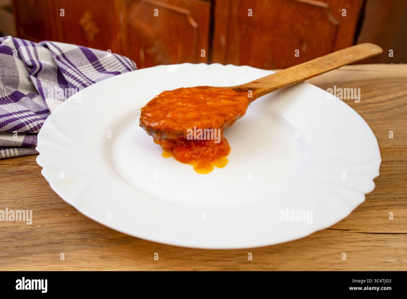 Marmellata di albicocche di colore arancione in un cucchiaio di legno pieno , su un piatto bianco, fuoco morbido Foto Stock
