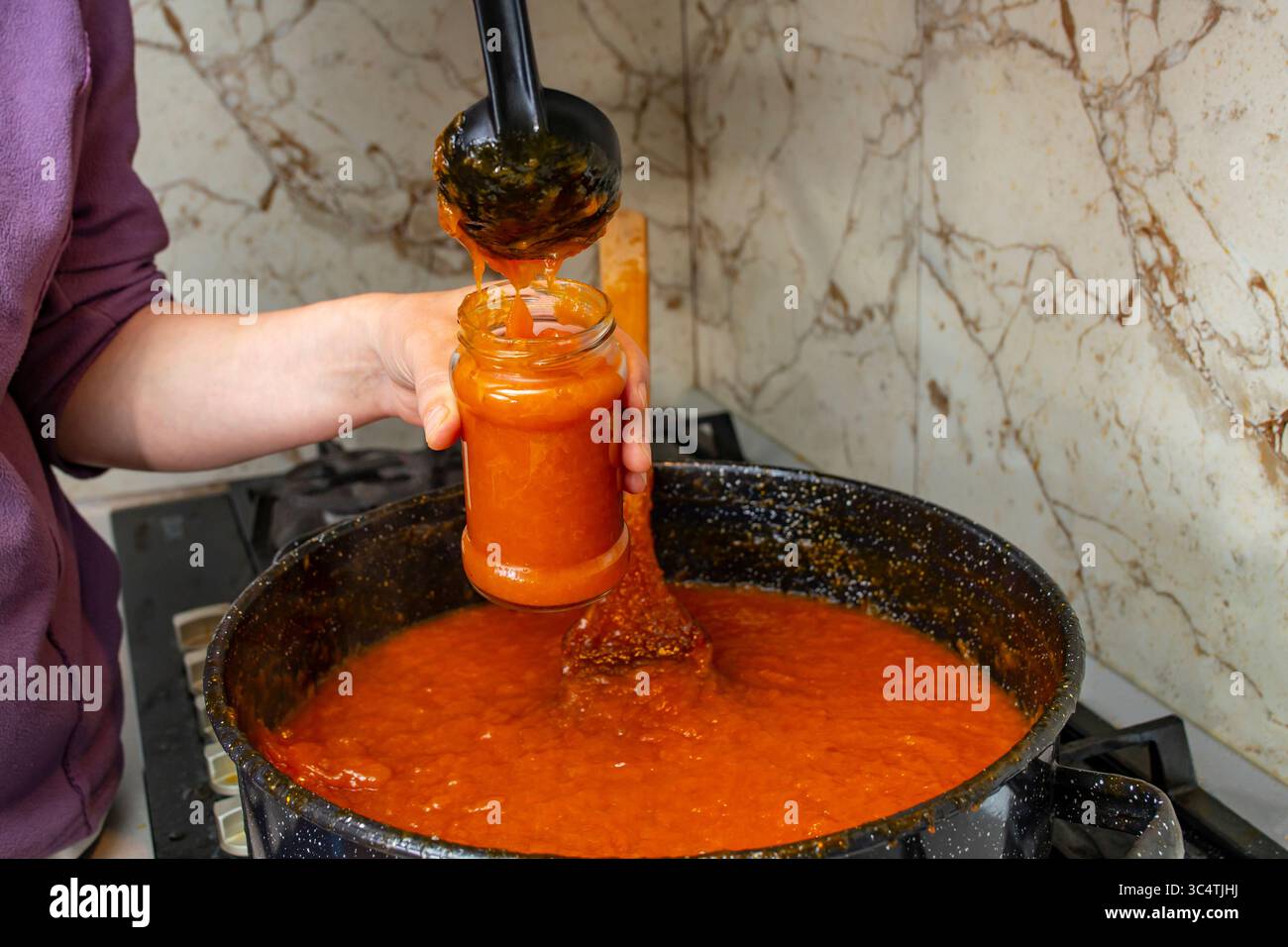 Mani di donna che porgono marmellata calda di albicocca o pesca in un vaso di vetro, con messa a fuoco morbida Foto Stock