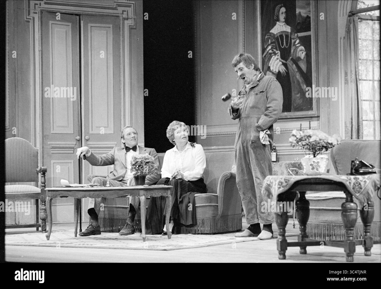 Play for the Elder IJmuiden, Theater, IJmuiden, Paesi Bassi, 24-02-1983 Whizgle News, Dutch Desk, Paesi Bassi, 1950-2000 Una scena teatrale con tre personaggi: un uomo in costume gesta animatamente, mentre una donna in camicetta ascolta con attenzione. Un altro uomo, vestito da tuta, ha uno strumento e sembra spiegargli qualcosa, con uno sfondo di arredi eleganti e un ritratto sul muro che aggiunge un'atmosfera all'ambiente. Foto Stock