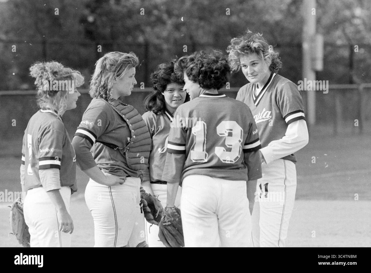 Softball Terrace Birds - Sparta, 19-05-1990 Whizgle News, Dutch Desk, Paesi Bassi, 1950-2000 Un gruppo di cinque giovani giocatori di softball si riuniscono sul campo, discutendo strategia e lavoro di squadra. Indossano maglie abbinate e le loro espressioni spaziano dall'attenzione all'amicizia, mettendo in risalto il loro spirito di cameratismo e competitivo. Foto Stock