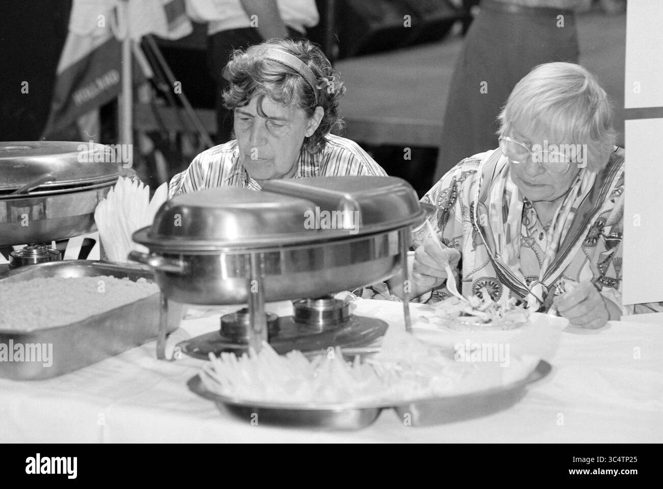 Bonte Beurs Beijneshal, 11-05-1994 Whizgle News, Dutch Desk, Paesi Bassi, 1950-2000 due persone sedute a un tavolo, focalizzate sui loro pasti. Sono circondate da vassoi pieni di cibo, a indicare un'esperienza culinaria comune. L'atmosfera suggerisce un raduno o un evento in cui condividere il cibo è fondamentale. Foto Stock