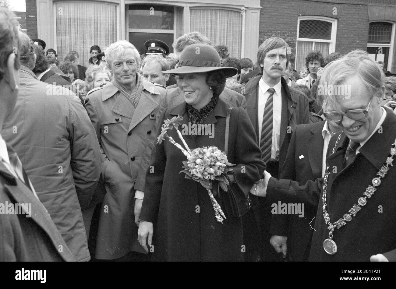 Regina Beatrice a Haarlem, ricevimenti reali e visite reali, Haarlem, Palmstraat, Paesi Bassi, 30-03-1983 Whizgle News, Dutch Desk, Paesi Bassi, 1950-2000 Una donna con un bouquet sorride mentre cammina attraverso una folla, accompagnata da funzionari e curiosi, creando una vivace scena di festa e coinvolgimento pubblico. Foto Stock